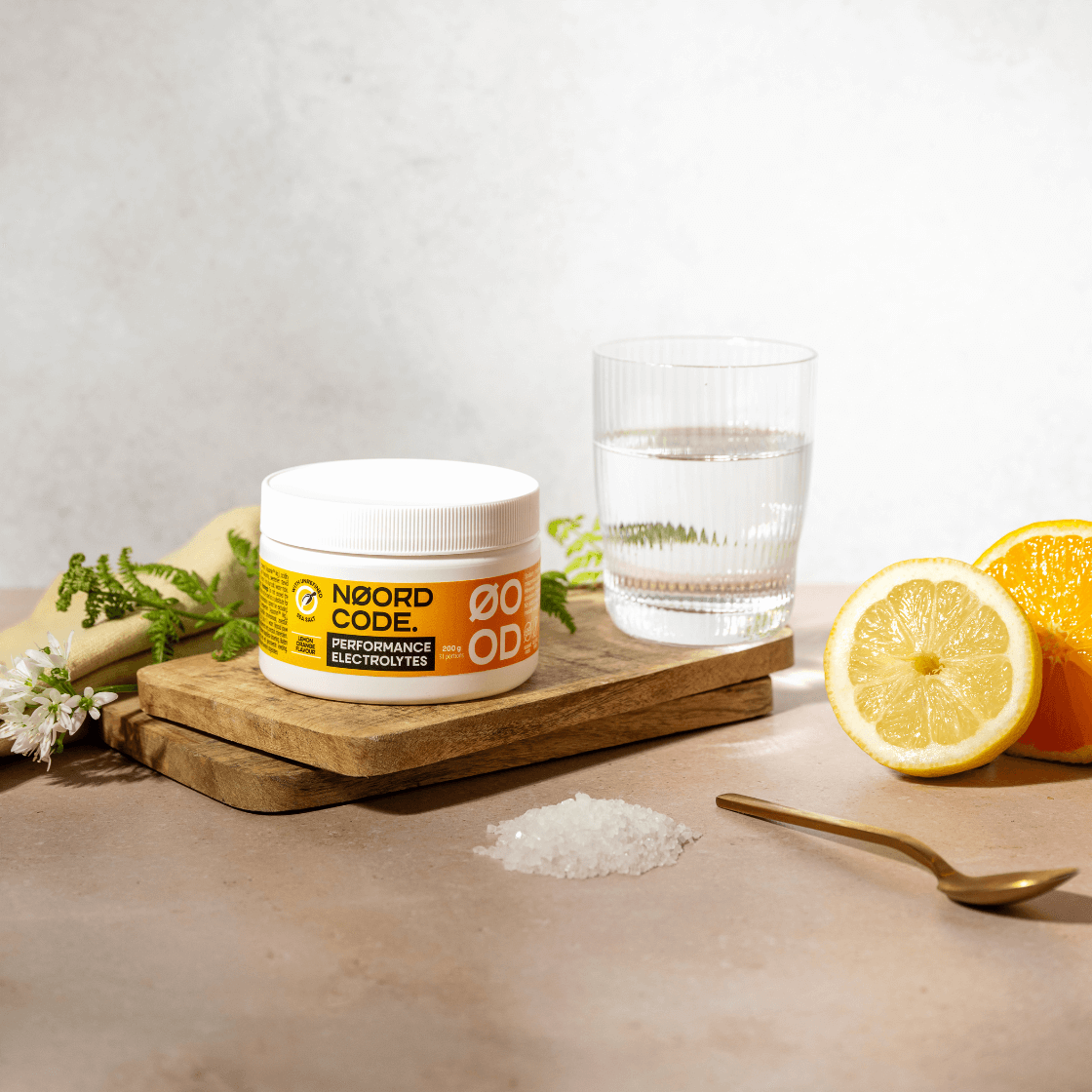 NoordCode Performance Electrolytes citrón–pomaranč – balenie elektrolytov z morskej soli na stole s vodou, citrónom, pomarančom a soľou.